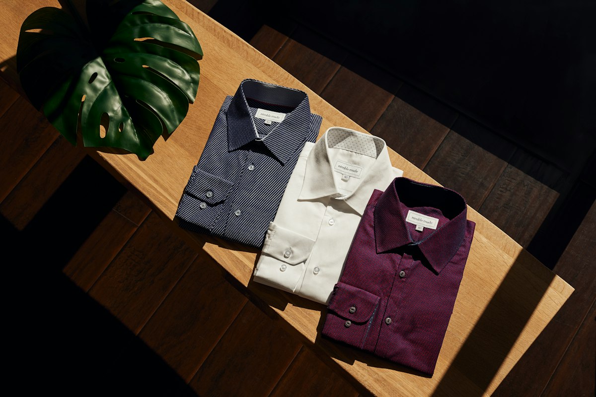 Folded men's dress shirts in navy, white and burgundy on a wooden table in warm light