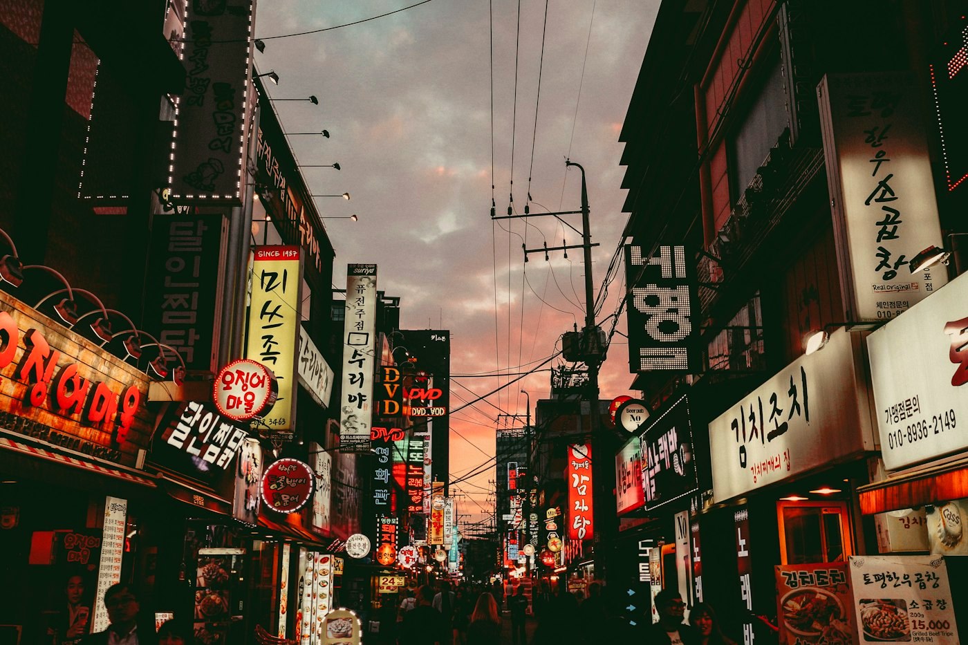 A Seoul shopping street at dusk under a pink sky